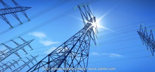 Strommasten im Sonnenlicht, erstmals liefert Photovoltaik in Deutschland Sekundärregelleistung zur Stabilisierung des Stromnetzes.