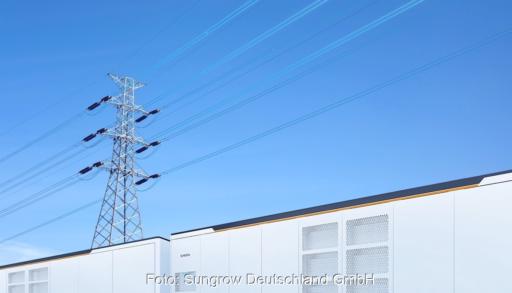 Ein im Vordergrund angeschnittener Batteriespeicher PowerTitan 2.0 in lichtgrau vor blauem Himmel. Im Hintergrund eine Strommast.
