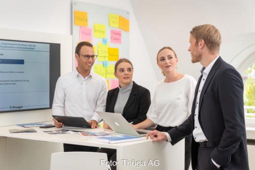 Mehrere Personen hören einem Vortragenden mit Laptop zu. Es geht um Beratung.