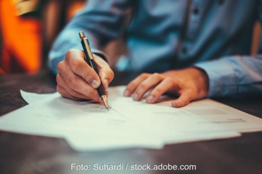 Person im Business-Hemd schreibt auf Formularen.