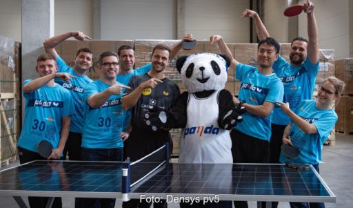 Timo Boll mit Stoff-Panda und Firmenvertreter:innen an einem als Tischtennisplatte aufgebauten Photovoltaik-Modul.