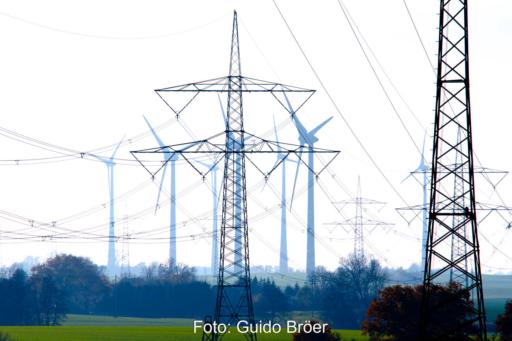 Hochspannungs-Strommasten im Vordergrund vor einem Windpark.
