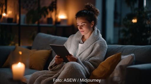 Frau mit Pad sitzt entspannt auf dem Sofa bei Kerzenschein.