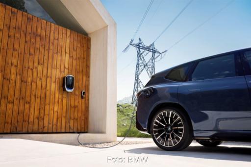 Elektrofahrzeug im Freienb an der Wallbox mit Hochspannungsmast in Sichtweite.