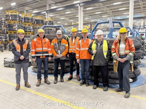 7 Personen in roten Schutzwesten in einer Halle mit Drahtrollen.