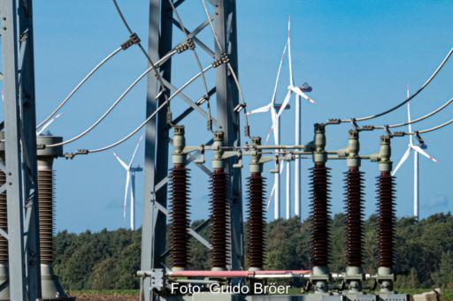 Durchsicht durch ein Umspannwerk auf einen Windpark. Im Vordergrund: Isolatoren, Strom- und Erdungsleitungen, Gittermasten.