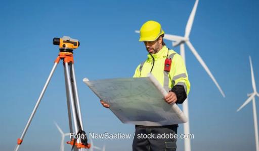 Ein Mann in Arbeitskleidung hält einen Plan vor Windenergieanlagen in den Händen, der TÜV hat den Windenergie-Ertragsgutachter Anemos-Jacob übernommen.