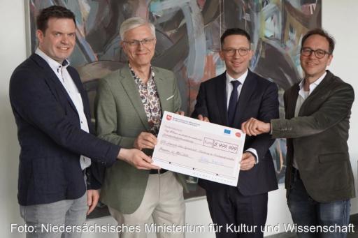 Vier Personen halten erfreut einen überdimensionierten Check über sechgs Millionen Euro in die Kamera.