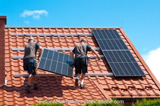 Zwei Männer tragen Photovoltaik-Modul auf Dach