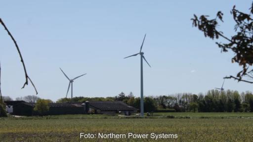 Eine Kleinwindanlage auf einem Hof in Schleswig-Holstein. Im Hintergrund eine Großwindkraftanlage.