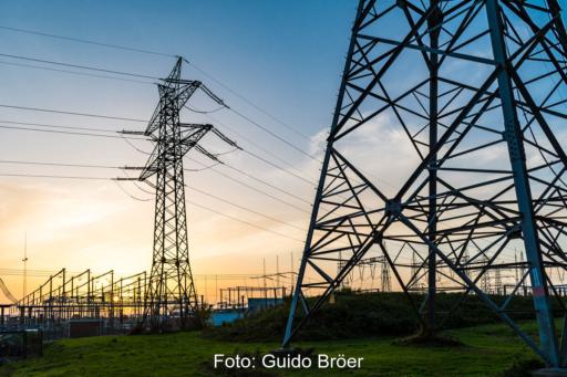 Sonnenuntergang hinter einem Umspannwerk. Im Vordergrund Hochspannungsmasten.