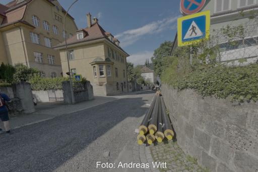 EIne Straße, an einer Mauer liegen Rohre für ein Wärmenetz.
