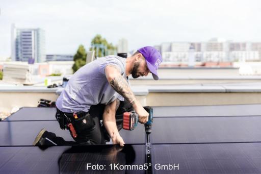 Das Foto zeigt einen Monteur mit einem Akku-Schrauber, der ein PV-Modul befestigt. Er trägt eine lila Kappe, ein fliederfarbenes T-Shirt sowie eine schwarze Arbeitshose. Er hockt neben dem Modul und ist von der Seite fotografiert.