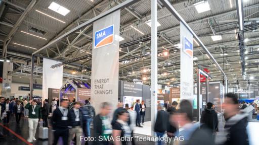 Das Foto zeigt einen Messestand in einer Halle mit davor vorbeilaufenden Menschen, die durch die Bewegung verschwommen sind.