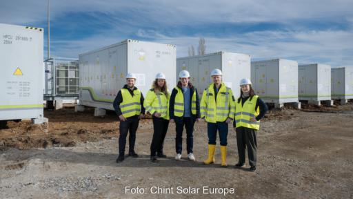 Das Bild zeigt fünf Personen mit weißen Schutzhelmen und neongelben Jacken und Westen vor mehreren Batteriespeicher-Systemen, schräg dahinter.