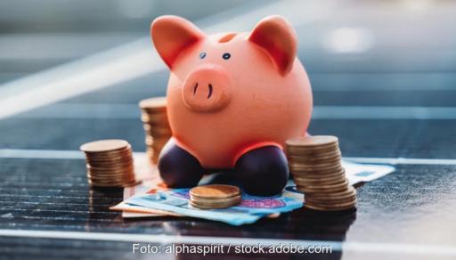 Ein Sparschwein mit Geld auf einem Solarmodul, Vattenfall bietet eine Finanzierung für Photovoltaik-Anlagen und Wärmepumpen an.