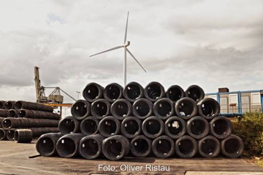 Stahldrähte auf riesigen Rollen, im Hintergrund eine Windenergie-Anlage - Symbol für Transformation der Industrie