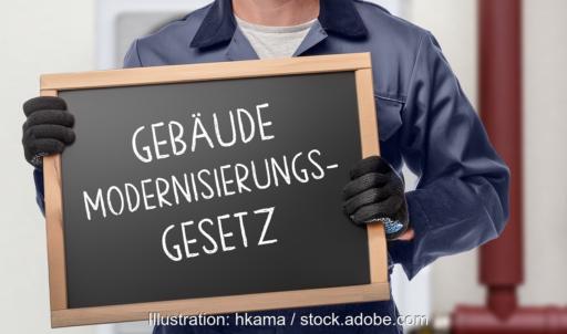 Ein Mensch hält eine Tafel mit der Aufschrift Gebäudemodernisierungsgesetz.