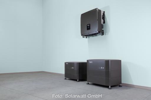 An einer Innenwand montierter Wechselrichter über zwei modularen Batteriespeichern von Solarwatt. Die Speichersysteme stehen auf dem Boden eines Technikraums und gehören zur neuen Heimspeicher-Generation Battery vision 2.0.