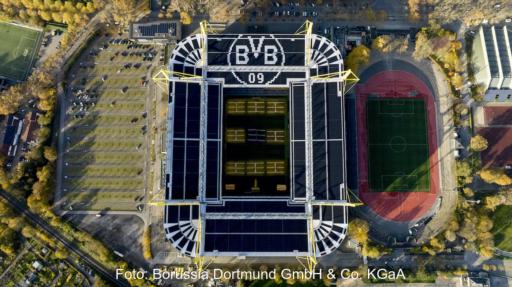 Senkrechte Luftaufnahme eines Fußballstadions. Auf den Dachflächen sind großflächig Photovoltaikmodule installiert. Neben dem Stadion sind Parkflächen und eine Leichtathletikanlage zu sehen.