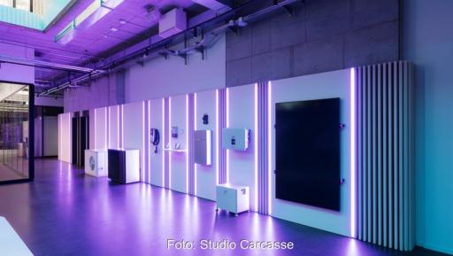 Ausstellungsfläche mit verschiedenen Energietechnik-Komponenten an einer beleuchteten Wand. Zu sehen sind unter anderem Geräte für Photovoltaik, Batteriespeicher, Wärmepumpen und Energiemanagement. Violette LED-Lichtstreifen und ein modernes Showroom-Design prägen die Szene.