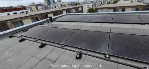 Auf einem Flachdach installierte PVT-Module in einem Wohnquartier. Die dunklen Hybridmodule sind in mehreren Reihen montiert. Im Hintergrund sind weitere Wohngebäude des Quartiers zu sehen.