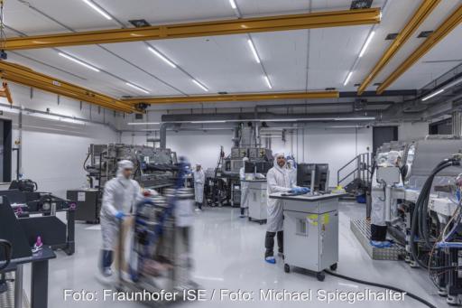 Blick in einem Raum des Fraunhofer ISE mit einigen kleinen Maschinen und Menschen, die sie bedienen. Hier finden praxisnahe Studien für die PV-Produktion statt.