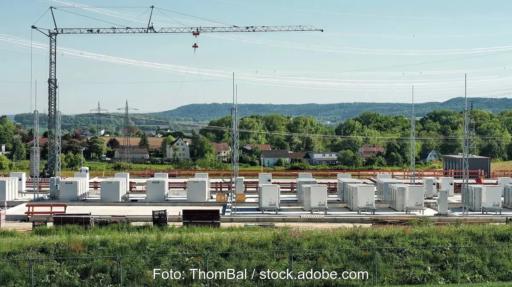 Kräne und Container auf grüner Wiese, ein Großbatteriespeicher-Park im Bau.