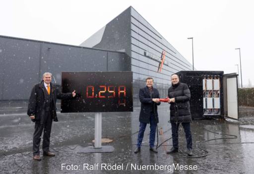 Der Personen mit großem Monitor und einem roten Stecker vor Messehallen in Nürnberg im Schneegestöber.