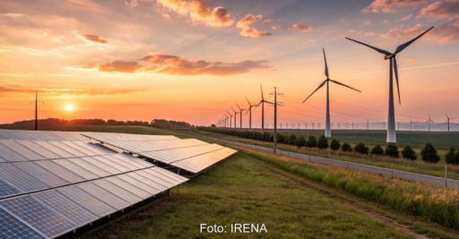 Große Freiflächen-Solaranlage im Vordergrund und mehrere Windkraftanlagen entlang einer Straße bei Sonnenuntergang.
