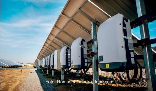 Rückseite mehrerer Solarmodule in einem Solarpark. An den Modulen sind Wechselrichter montiert, die den erzeugten Gleichstrom in Wechselstrom umwandeln.