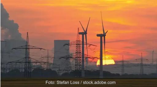 Windenergieanlagen, Strommasten und ein fossiles Kraftwerk liegen in einem orange-roten Sonnenuntergang.