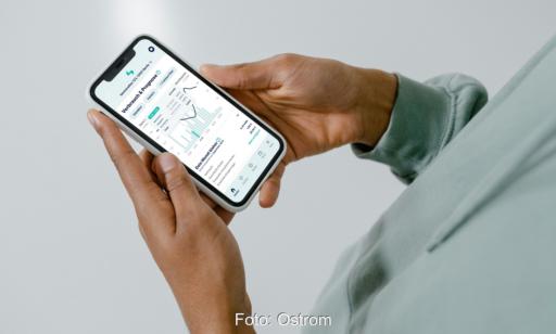 Im Bild Hände, die ein Handy halten, auf der die App von Ostrom mit dem virtuellen Kraftwerk Neogrid AI läuft.