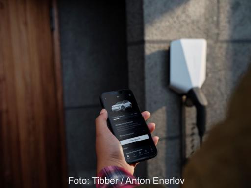 Hand hält Smartphone mit offener App zum Laden eines E-Autos - Wallbox im Hintergrund.