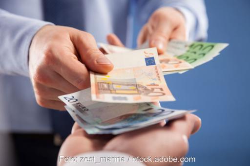 Die Hände einer Person zählen Geldscheine in die Hände einer zweiten Person.
