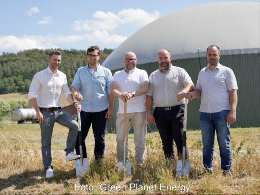 5 Personen mit Spaten vor einem Biogasbehälter.