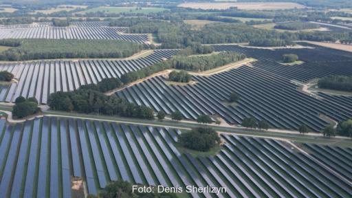 Luftaufnahme eines großflächigen Solarparks mit langen Reihen von Photovoltaik-Modulen zwischen Baumgruppen, Straßen und landwirtschaftlichen Flächen.
