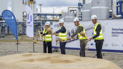 Vier Personen mit weißen Schutzhelmen und neongelben Warnwesten beim Spatenstich für die SOEC-Testanlage im Industriepark Lausitz in Schwarzheide.