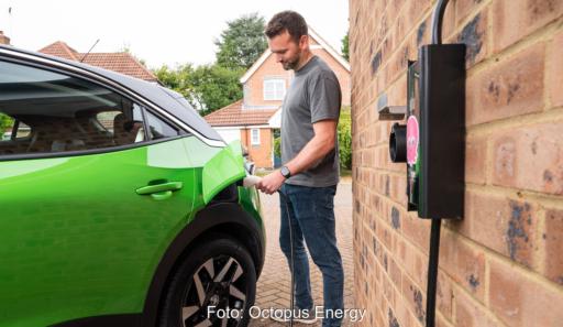 Ein Mann schließt ein grünes Elektroauto an eine Wallbox an einer Hauswand an.
