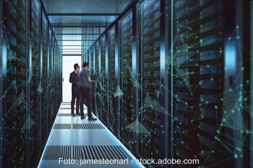 Zwei Männer im Gang eines Rechenzentrums zwischen Computer- oder Speicher-Racks hinter Glas, wobei das Foto im bläulichen Licht an eine Science-Fiction-Umgebung erinnert.