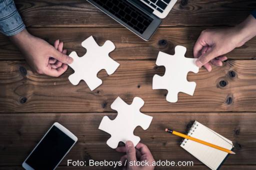 Fokus auf drei große Puzzleteile, von Fingern gehalten und Taschenrechnern und Computern.
