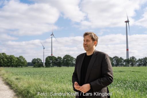 Bundesfinanzminister Lars Klingbeil im Vordergrund. Im Hintergrund Windkraftanlagen.