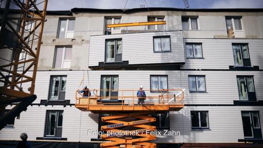 Ein Kran hebt Bauelemente an die Fassade, serielle Sanierung mit vorgefertigten Holzständerelementen.