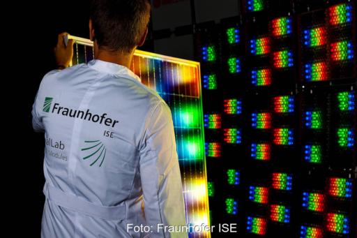 Mitarbeiter des Fraunhofer ISE hält ein PV-Modul vor einen multispektralen Sonnensimulator mit roten, grünen und blauen LEDs.