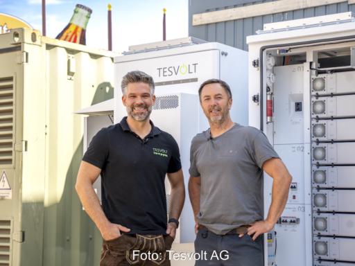 Zwei Männer stehen vor zwei weißen Tesvolt-Batteriespeichern auf dem Gelände des Münchner Oktoberfests; einer der Speicher ist geöffnet.