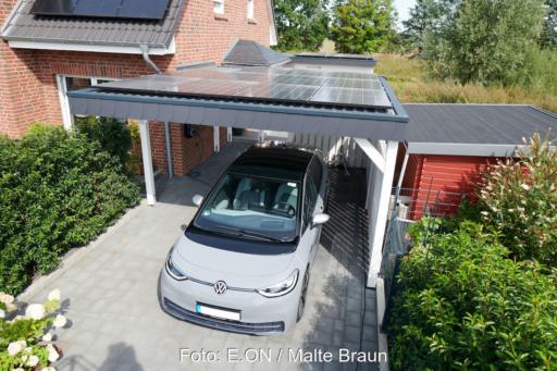 Graues Elektroauto unter einem mit Solarmodulen belegten Carport vor einem Backsteinhaus mit weiterer Photovoltaikanlage.