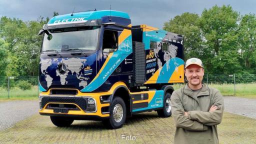 Tobias Wagner steht vor dem blau-orange folierten Elektro-Lkw eActros 600 mit Wohnmobil-Aufbau und Weltkartenmotiv.