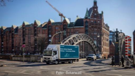 LKW mit Solarwatt-Schriftzug fährt über historische Brücke vor alten Backsteinhäusern - PV-Installation in Hamburg
