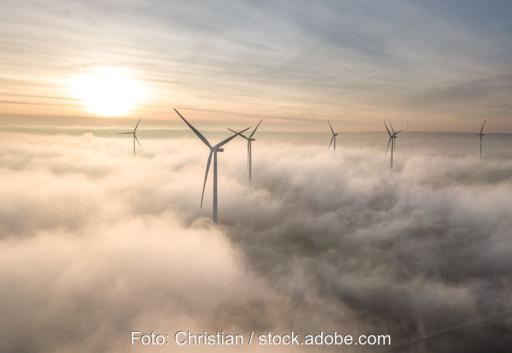 Windenergieanlagen an Land bei Sonnenaufgang und aufsteigendem Dunst.