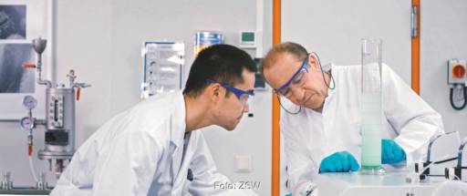 Zwei Männer mit Schutzbrillen arbeiten an einem Glaskolben, in dem eine grüne Flüssigkeit ist - Material für die Natrium-Ionen-Batterie